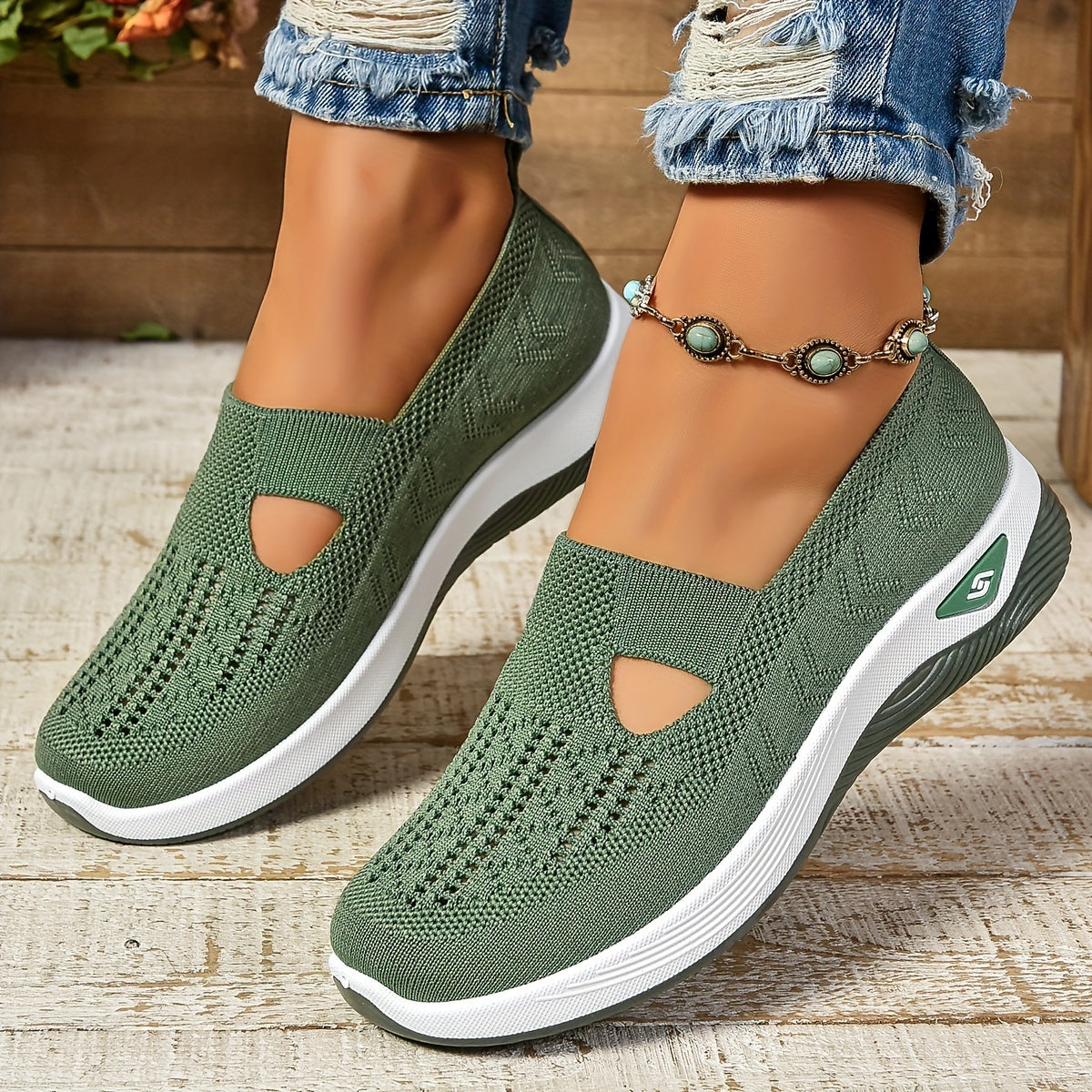 Green slip-on shoes with white soles worn by a person on a wooden floor.
