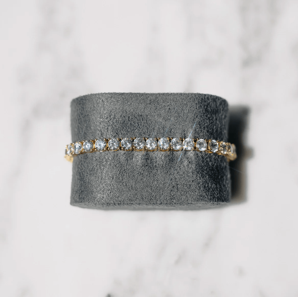 Elegant diamond tennis bracelet on gray velvet, featuring sparkling round-cut diamonds set in gold, perfect for luxury jewelry enthusiasts.