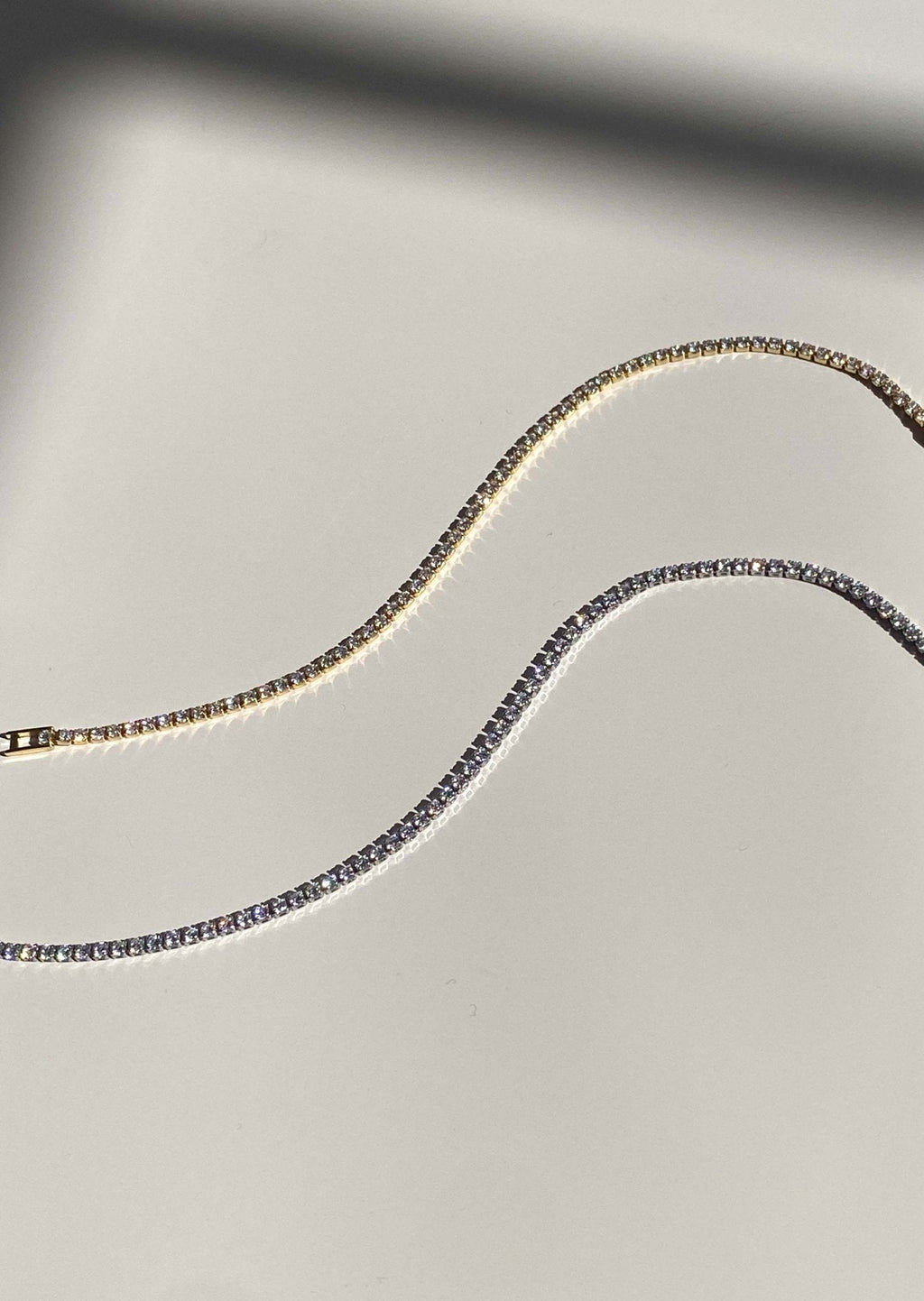 Elegant gold and silver tennis bracelets on a reflective surface, showcasing sparkling gemstones. Luxury jewelry, fashion accessories, stylish design.