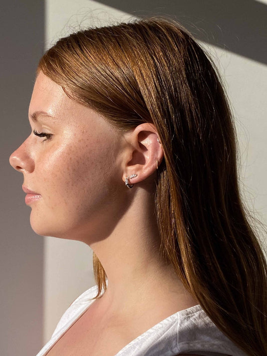 Profile of a woman with red hair and freckles, wearing a white top and silver earrings, in natural sunlight.