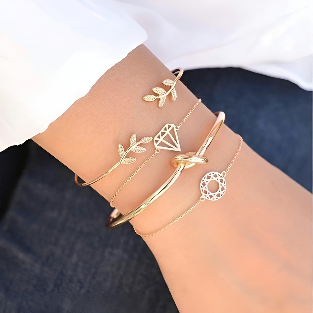 Elegant gold bracelets on wrist, featuring leaf, diamond, knot, and circle designs. Fashionable jewelry accessories for women.