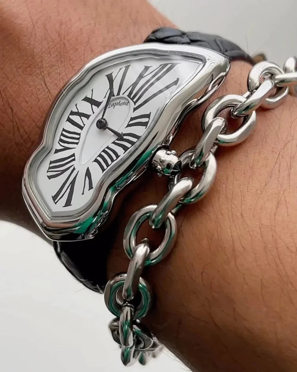 Silver watch with Roman numerals on a wrist, wearing a matching silver chain bracelet.