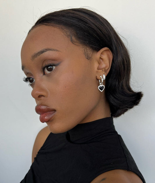 Young woman with sleek bob hairstyle wearing heart-shaped silver earrings and a black turtleneck, showcasing elegant fashion and beauty style.
