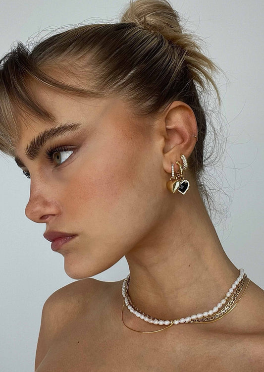 Woman with multiple gold hoop earrings and heart-shaped pendant, wearing layered necklaces. Fashion jewelry, trendy accessories, side profile.