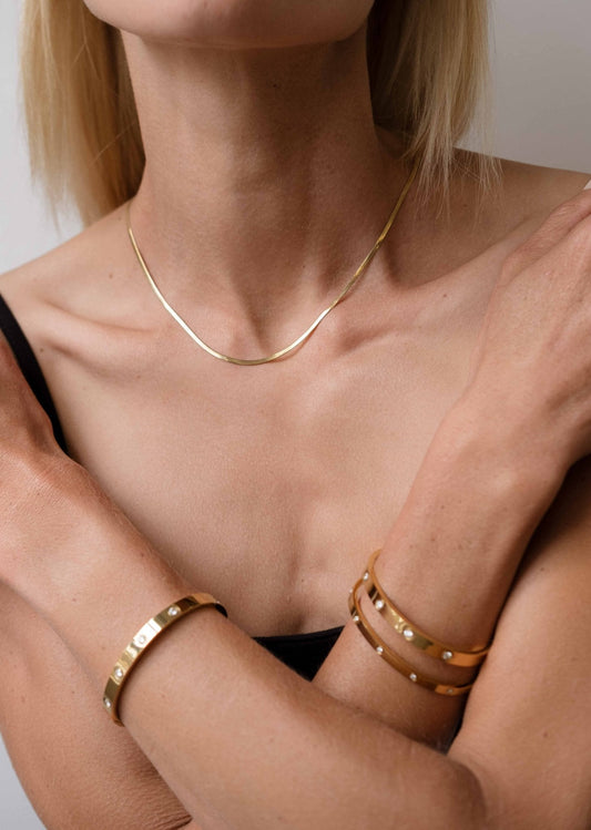 Woman wearing a gold necklace and leather bracelets, showcasing minimalist jewelry fashion. Close-up of accessories on bare shoulders and arms.