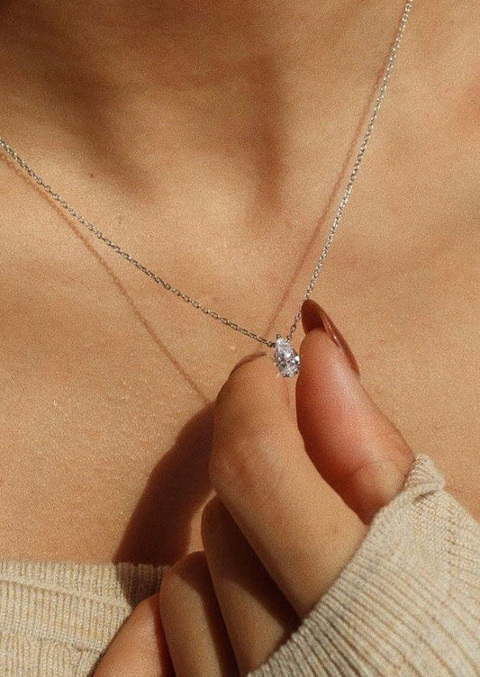 Elegant silver necklace with a sparkling diamond pendant held by a woman's hand, showcasing minimalist jewelry fashion against a warm skin tone background.