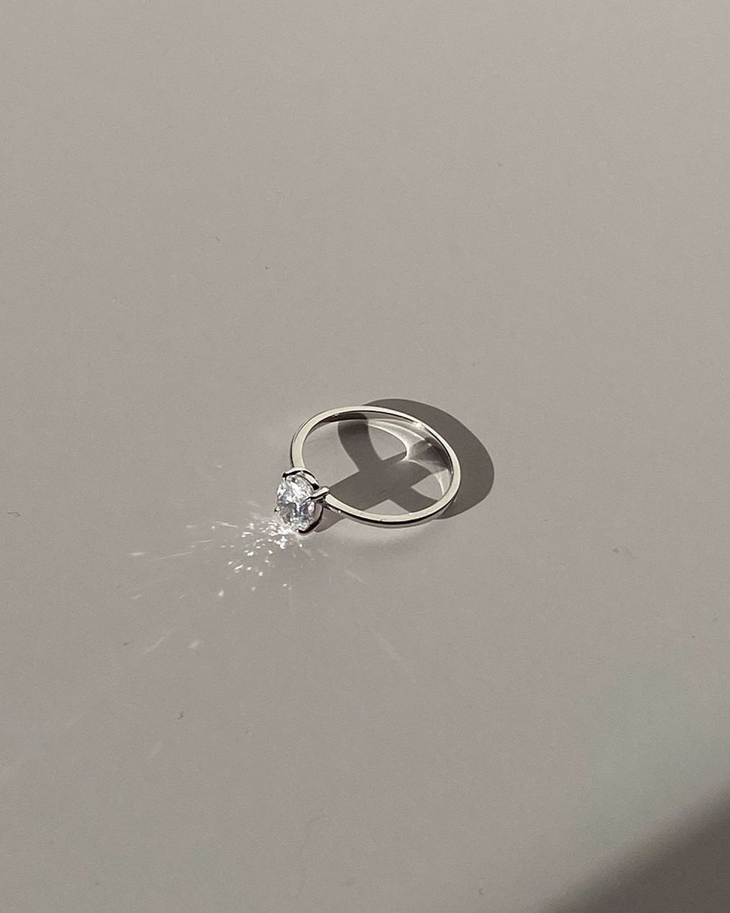 Elegant silver engagement ring with a sparkling solitaire diamond on a minimalist gray background, showcasing luxury jewelry design and craftsmanship.