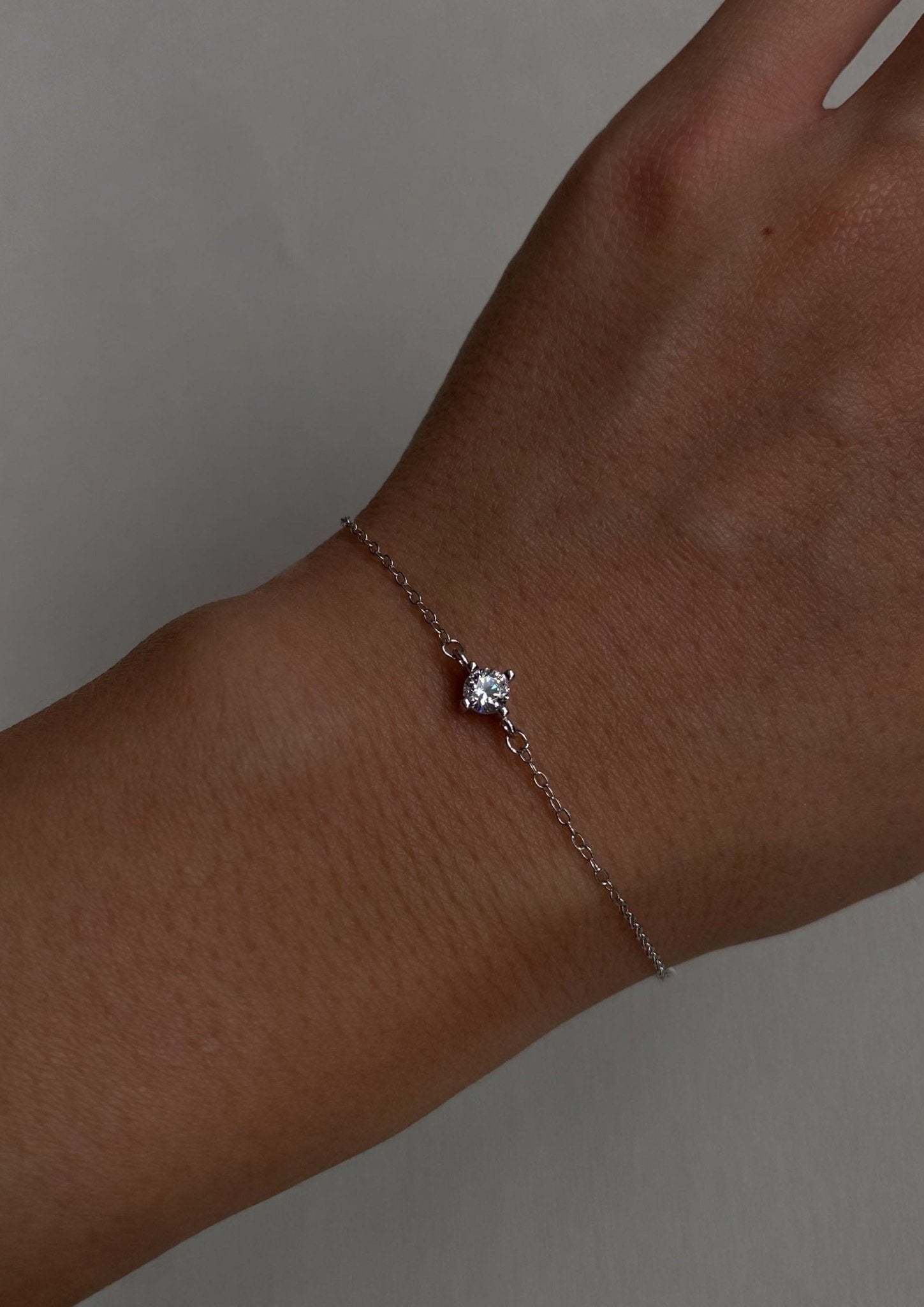 Delicate silver chain bracelet with a single sparkling diamond on a wrist, minimalist jewelry, elegant accessory, close-up.