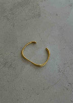 Gold open cuff bracelet on textured gray surface, minimalist jewelry design, elegant fashion accessory, modern style, unisex wristwear.