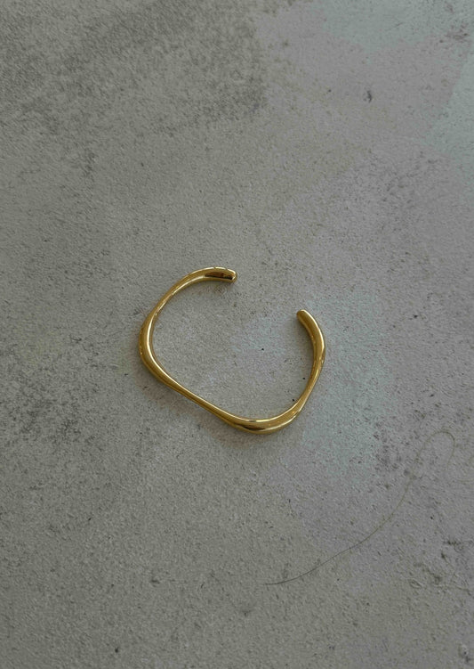 Gold open cuff bracelet on textured gray surface, minimalist jewelry design, elegant fashion accessory, modern style, unisex wristwear.