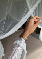 Hand with gold and silver bangles in front of a white lace canopy bed, showcasing elegant jewelry and bedroom decor.