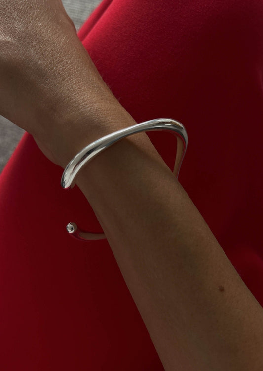 Elegant silver bracelet on a woman's wrist against a vibrant red background, showcasing minimalist jewelry design and modern fashion accessory trends.