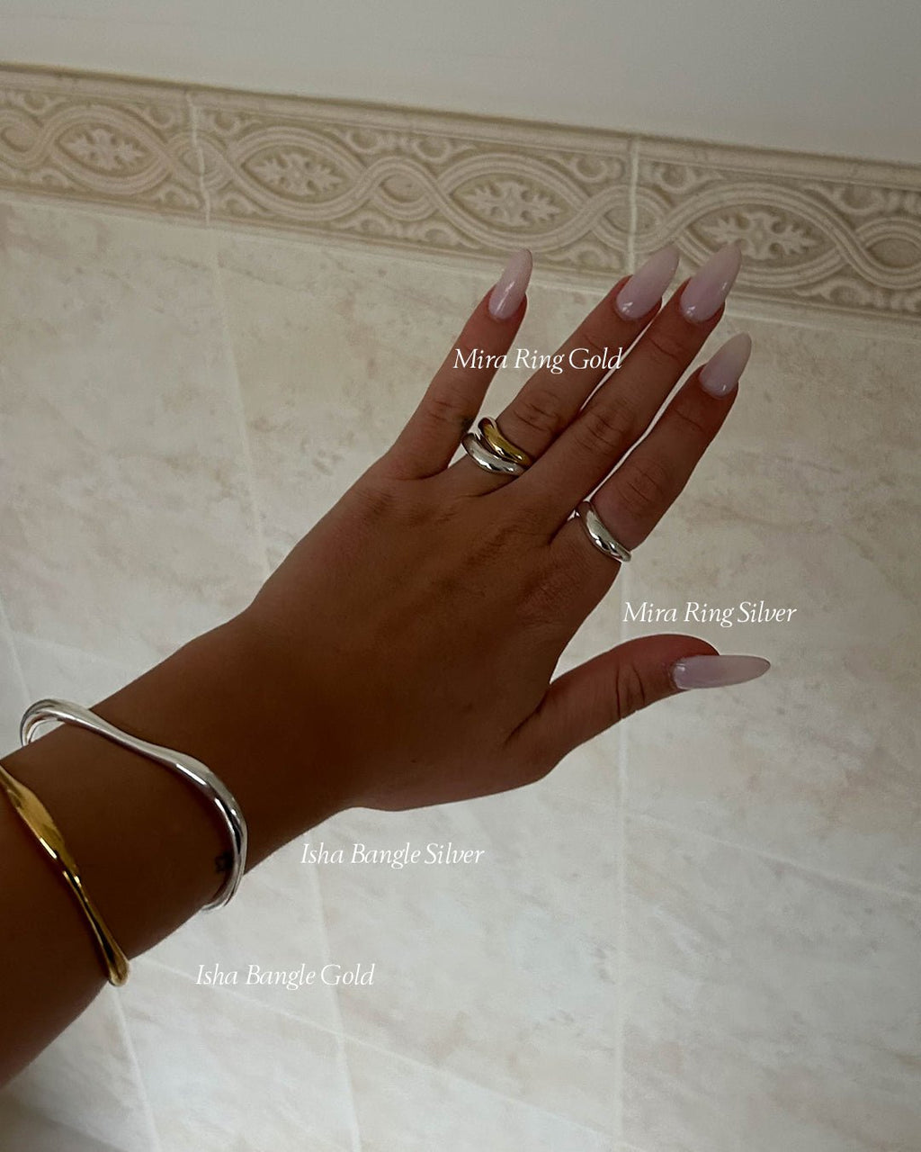 Hand adorned with gold and silver rings and bangles, showcasing elegant jewelry against a neutral tiled background.