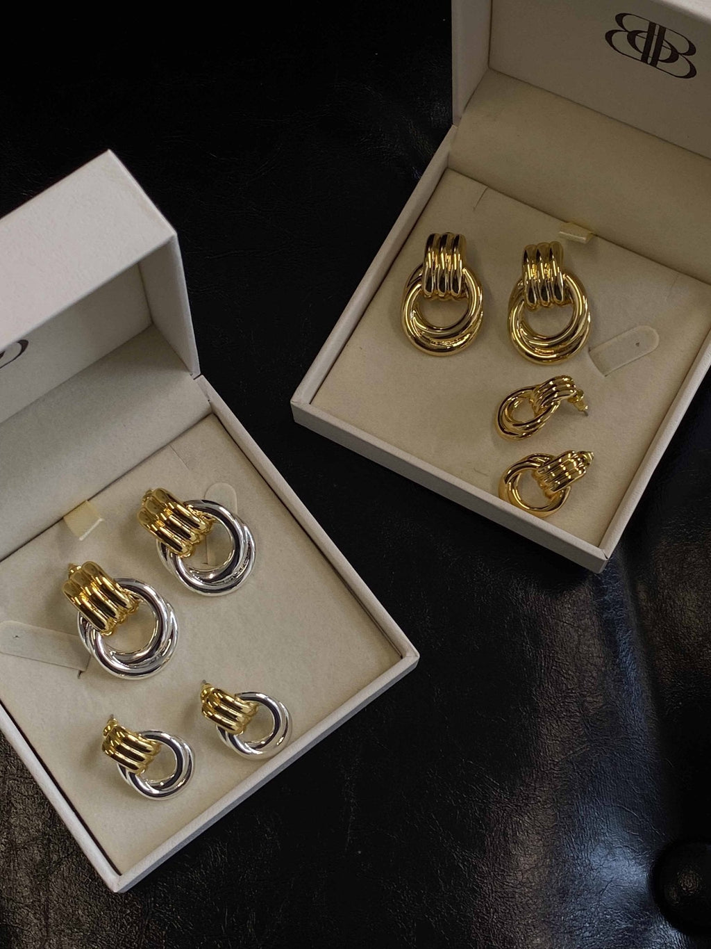 Gold and silver hoop earrings set in open jewelry boxes on black leather background, showcasing elegant, luxury fashion accessories.