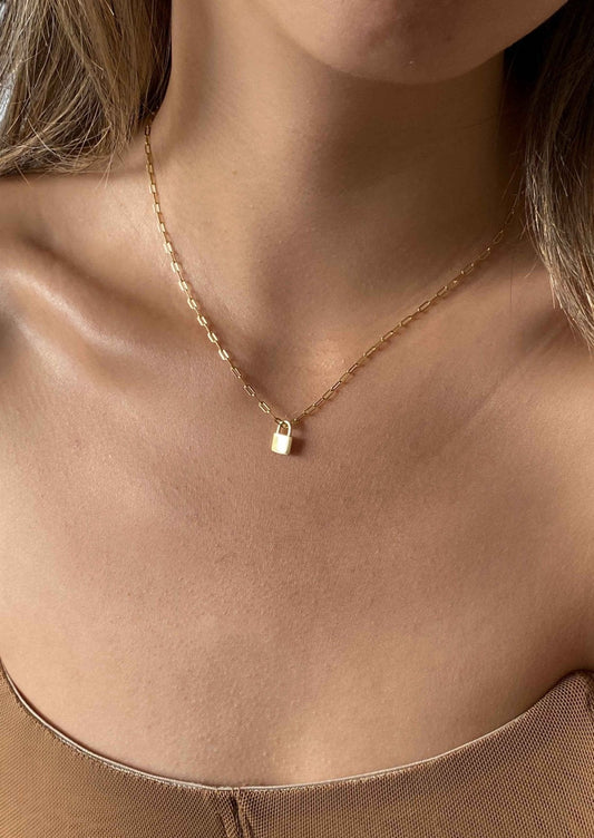 Gold chain necklace with a small padlock pendant on a woman's neck, close-up. Elegant jewelry, minimalist fashion accessory, delicate design.