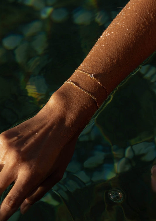 Hand with delicate gold bracelets submerged in clear water, glistening in sunlight. Elegant jewelry, summer fashion, aquatic background.