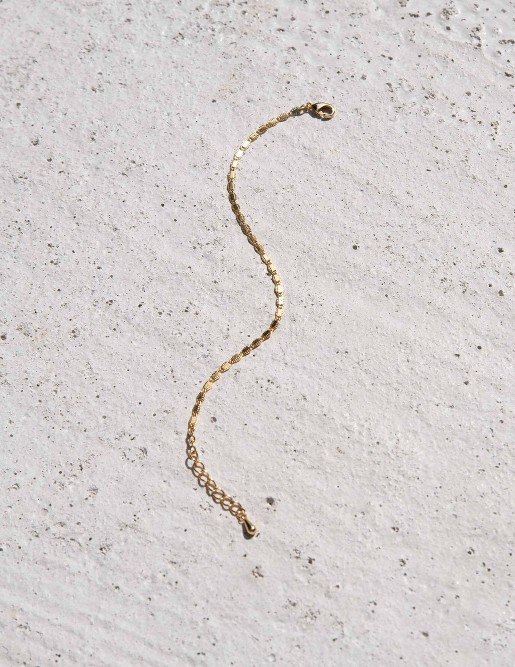Gold chain bracelet on textured concrete background, minimalist jewelry, elegant accessory, fashion statement, simple design, luxury style.