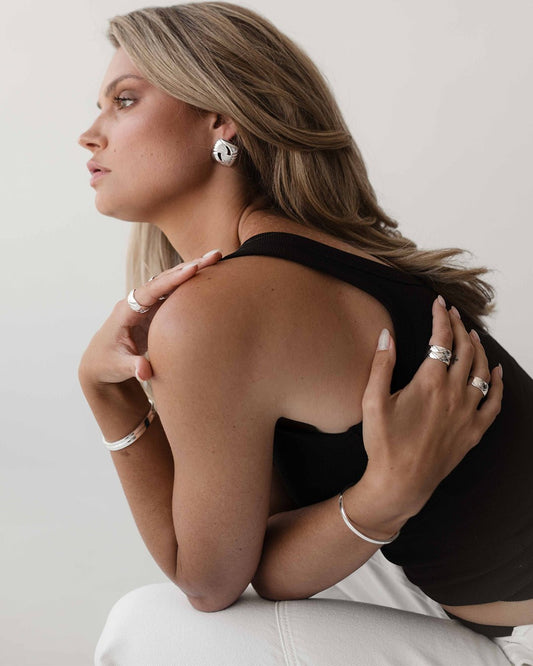 Woman wearing silver jewelry, including earrings, rings, and bracelets, in a stylish pose. Fashion accessories, elegant design, modern style.