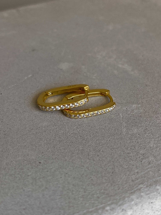 Gold hoop earrings with sparkling diamonds on a textured gray surface, luxury jewelry, elegant accessory, fashion statement, gift idea.