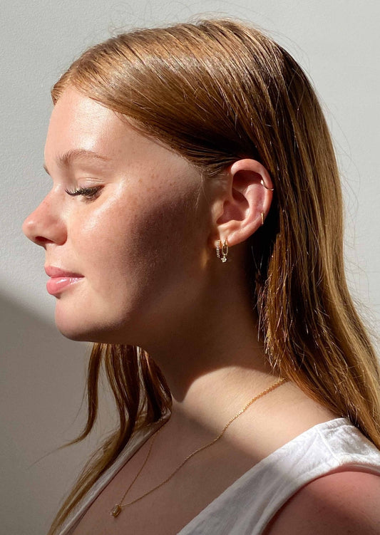 Young woman with red hair and gold hoop earrings, wearing a white top, side profile in natural light. Fashion, jewelry, and beauty concept.