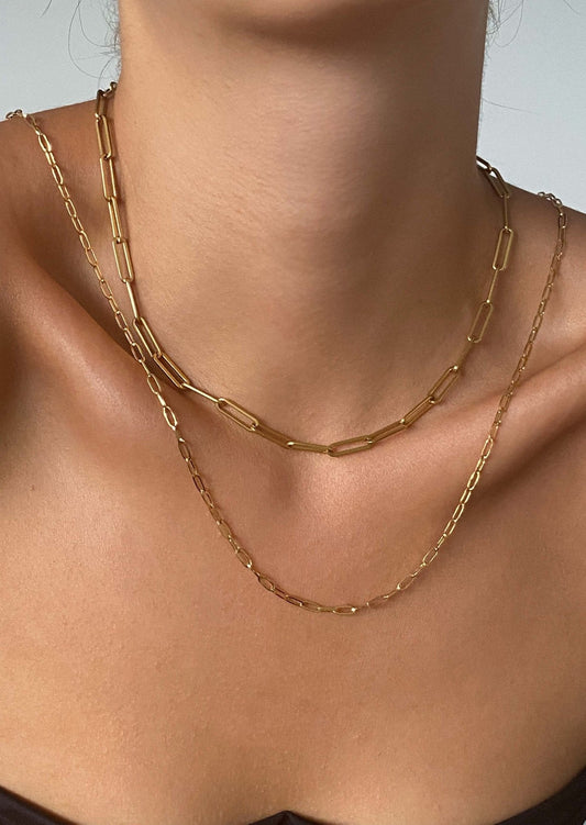 Gold paperclip chain necklaces on woman's neck, minimalist jewelry, layered fashion accessory, elegant style, close-up.