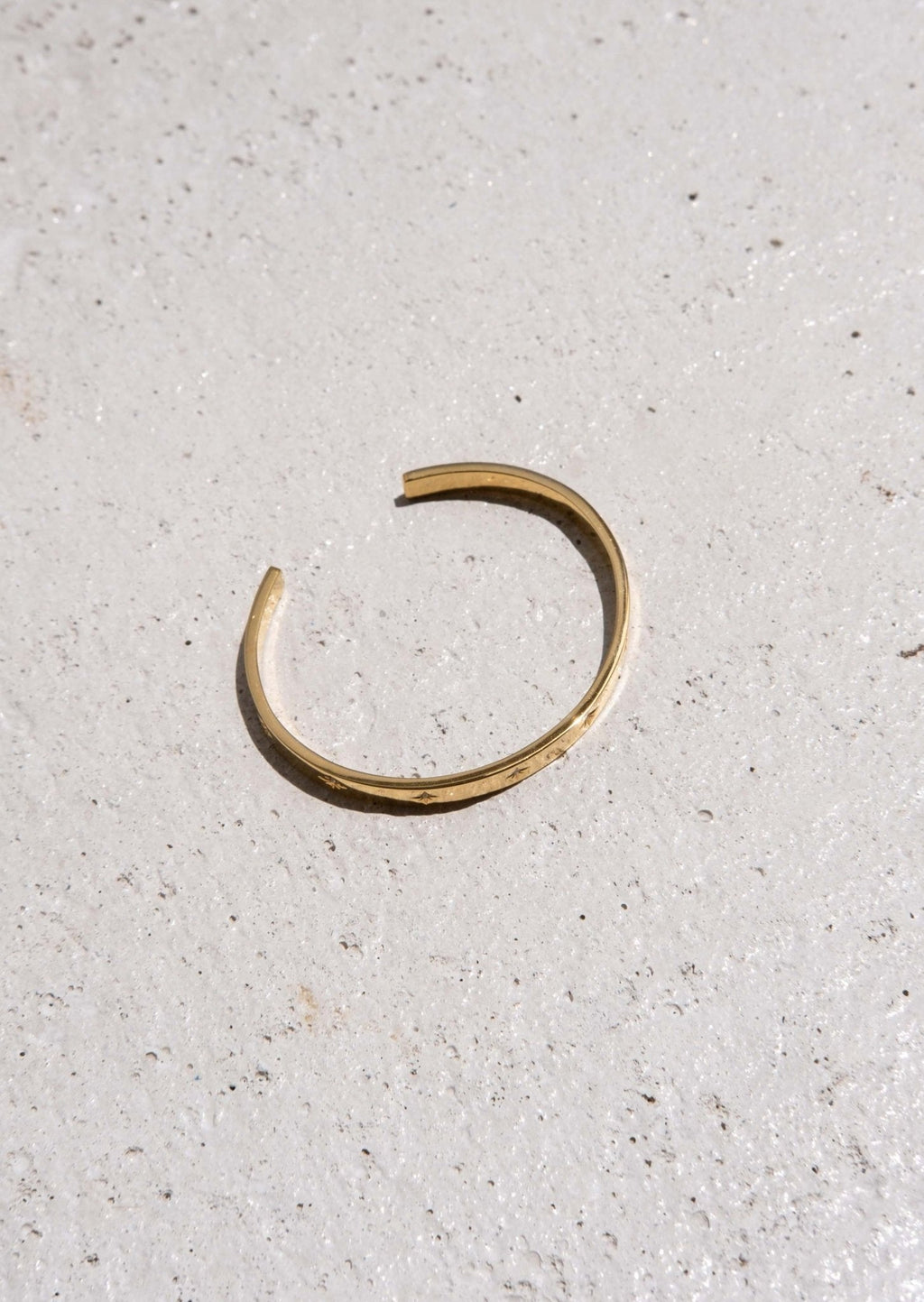Minimalist gold open cuff bracelet on textured concrete surface, showcasing elegant jewelry design, fashion accessory, modern style.