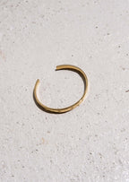 Minimalist gold open cuff bracelet on textured concrete surface, showcasing elegant jewelry design, fashion accessory, modern style.