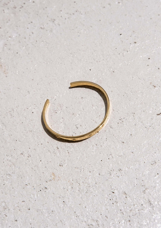 Minimalist gold open cuff bracelet on textured concrete surface, showcasing elegant jewelry design, fashion accessory, modern style.