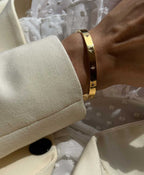 Gold star-embellished bracelet on wrist, worn over a cream blazer sleeve, showcasing elegant fashion accessory style and luxury jewelry trends.