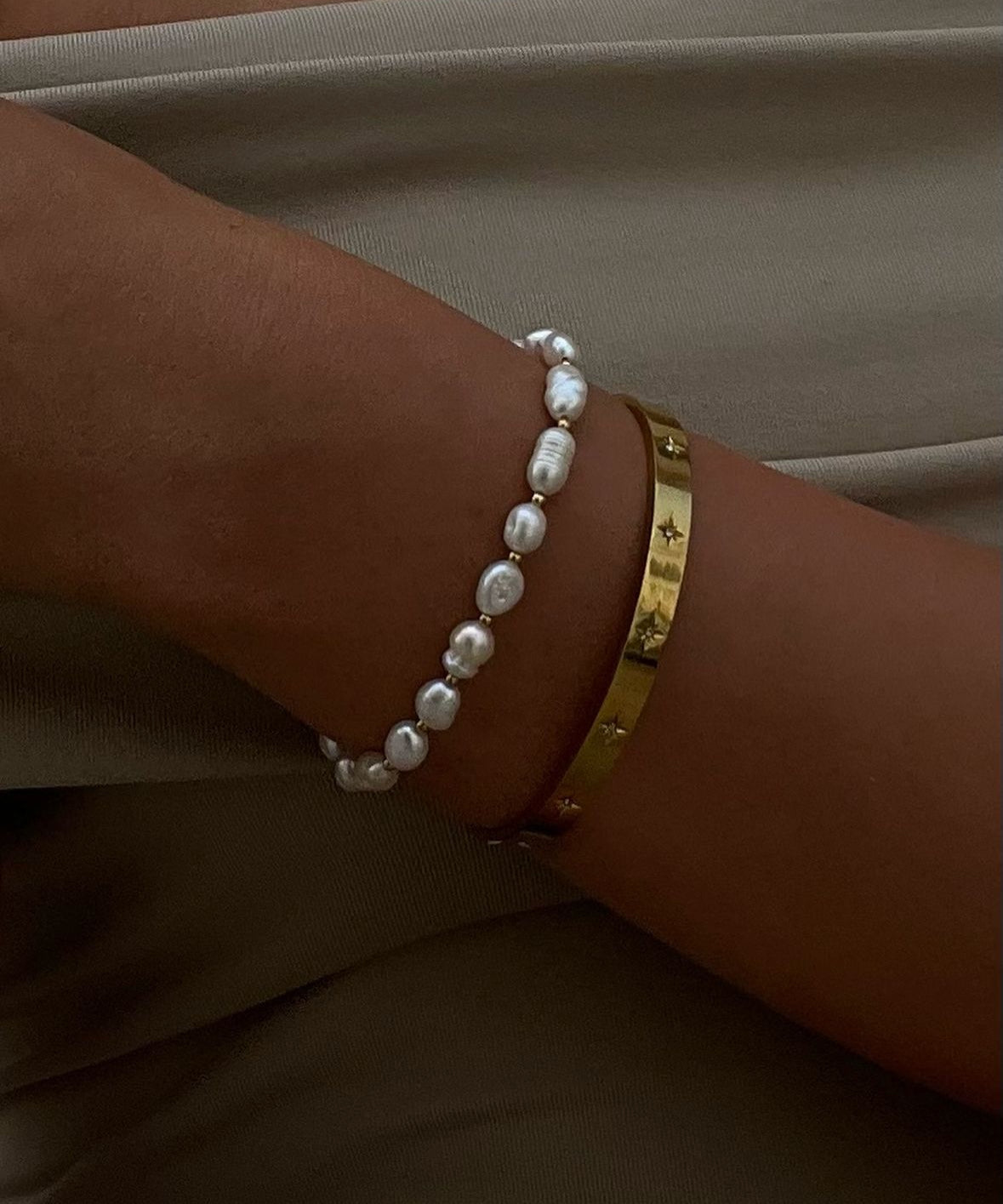 Elegant wrist adorned with a gold bangle and a pearl bracelet, showcasing luxury jewelry fashion. Perfect for style and accessory enthusiasts.