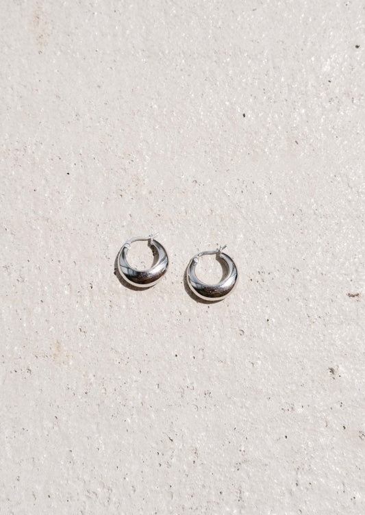 Silver hoop earrings on textured white background, minimalist jewelry, fashion accessories, small round hoops, elegant design, women's earrings.