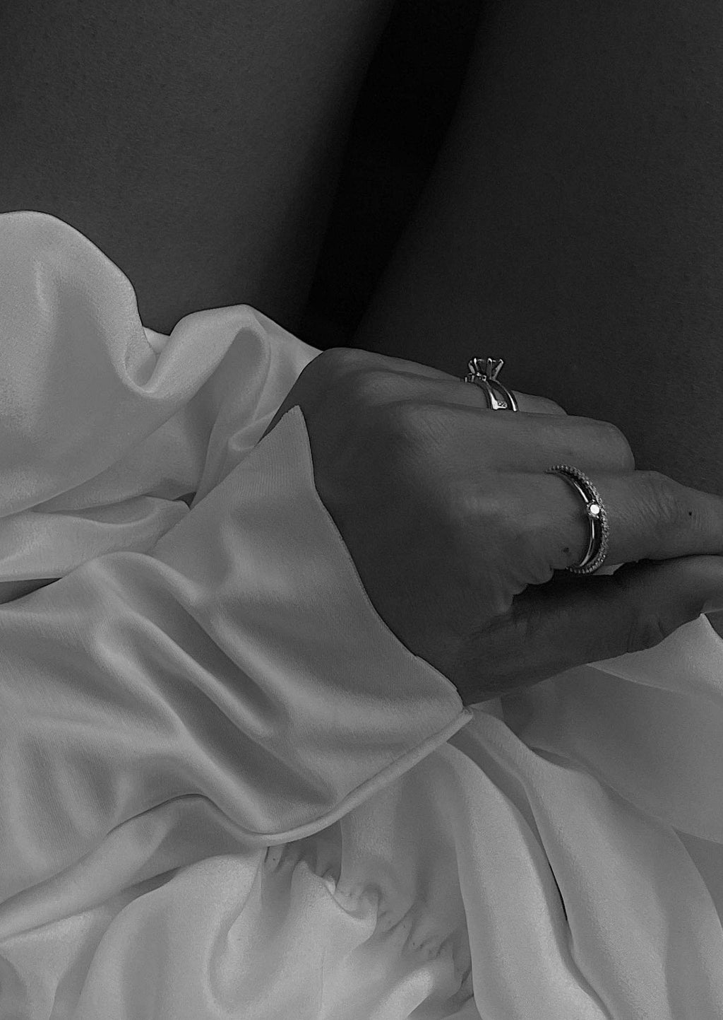 Close-up of a hand wearing elegant rings, resting on a silky white fabric. Fashion jewelry, luxury accessories, and style concept. Black and white.