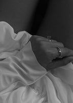 Close-up of a hand wearing elegant rings, resting on a silky white fabric. Fashion jewelry, luxury accessories, and style concept. Black and white.