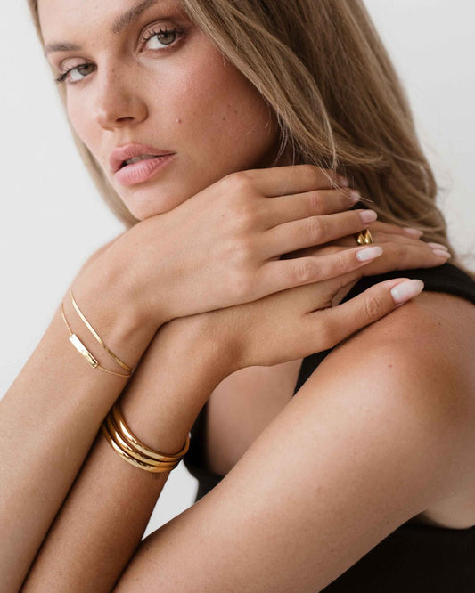 Woman wearing gold bracelets and ring, showcasing elegant jewelry on her hands and arms, with a neutral background. Fashion accessories close-up.