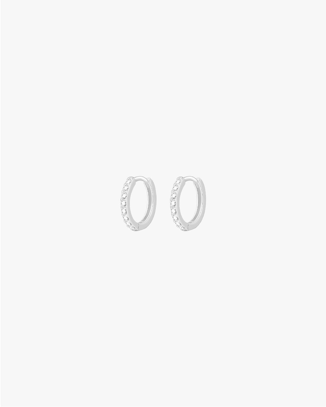 Silver hoop earrings with small embedded crystals on a white background, minimalist jewelry, elegant accessory, women's fashion, sparkling design.