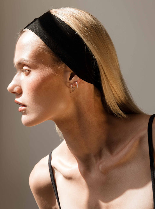 Profile of a woman with blonde hair wearing a black headband and earrings, in natural light. Fashion portrait, minimalist style, side view.