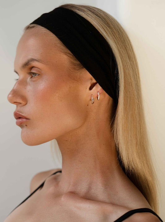 Profile of a woman with long blonde hair wearing a black headband and silver hoop earrings, showcasing minimalist fashion and beauty style.