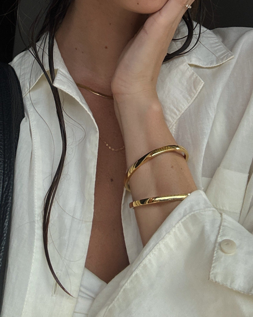 Woman in white linen shirt with wet hair, wearing gold bangles and a delicate necklace, showcasing minimalist fashion and jewelry style.