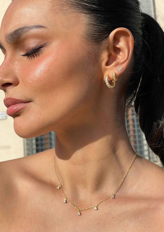 Woman wearing gold hoop earrings and a delicate gold necklace with small charms, showcasing elegant jewelry fashion.