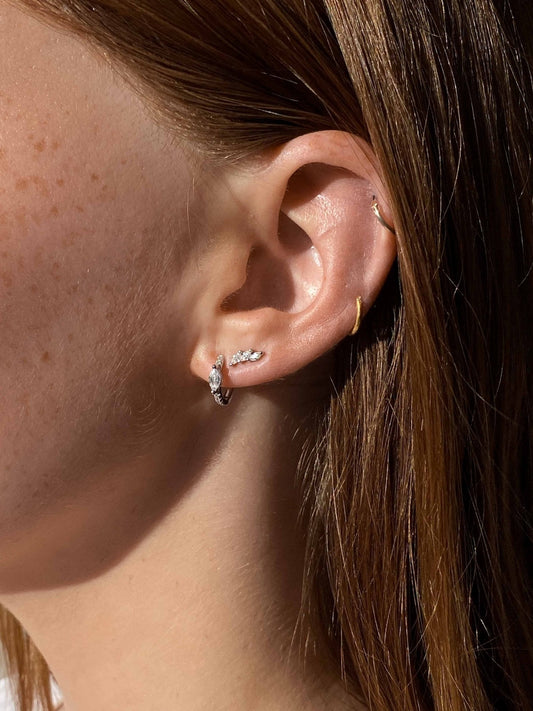 Close-up of a woman's ear with multiple piercings, featuring silver hoop and stud earrings. Jewelry fashion, ear piercing trends, minimalist style.
