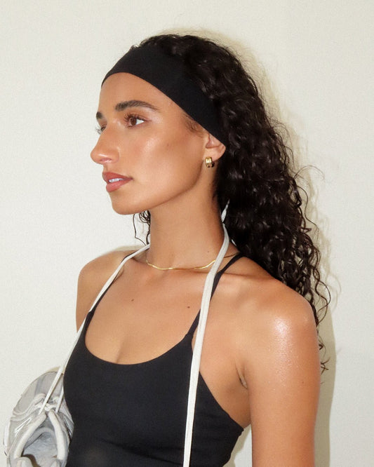 Young woman with curly hair wearing a black headband and tank top, holding a white bag. Fitness fashion, athletic style, healthy lifestyle.
