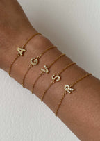 Gold initial bracelets with letters A, C, V, Y, R on a wrist, featuring delicate chains and sparkling letter charms. Perfect personalized jewelry gift.
