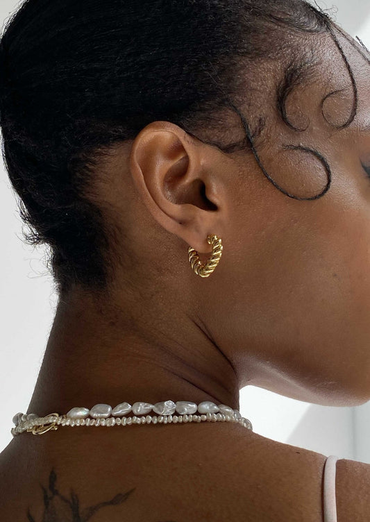 Close-up of a woman wearing a gold twisted hoop earring and a pearl necklace, showcasing elegant jewelry fashion.