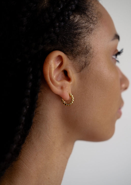 Close-up of a woman's ear wearing a small gold twisted hoop earring, showcasing elegant jewelry fashion.