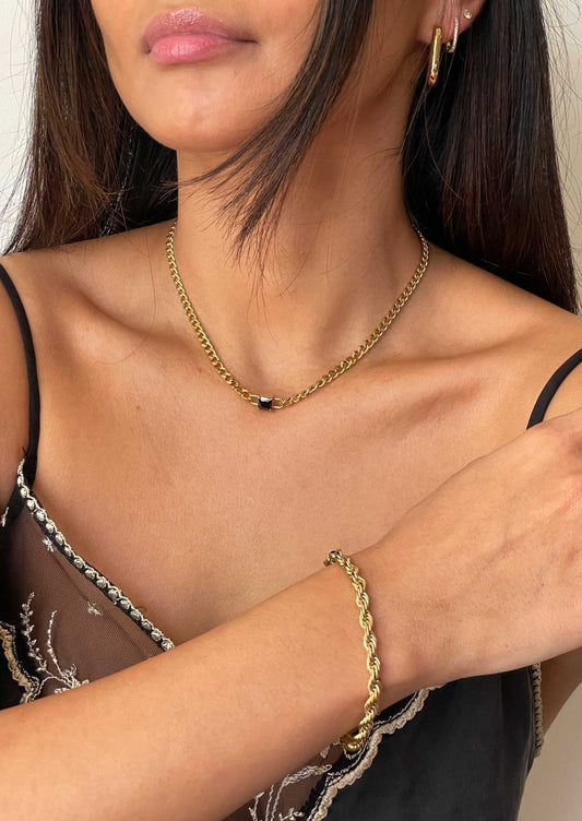 Woman wearing gold chain necklace and bracelet, black camisole with lace details, and gold hoop earrings. Fashion jewelry and accessories.