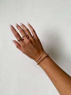 Elegant hand with manicured nails wearing gold rings and bracelets on a white background. Fashion jewelry, minimalist style, women's accessories.