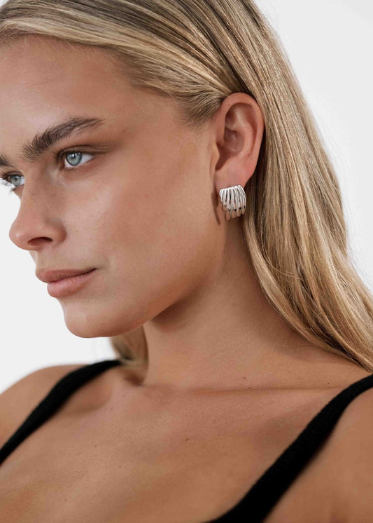 Woman wearing silver hoop earrings, close-up profile. Blonde hair, black top, minimalist jewelry. Fashion accessory, elegant style.