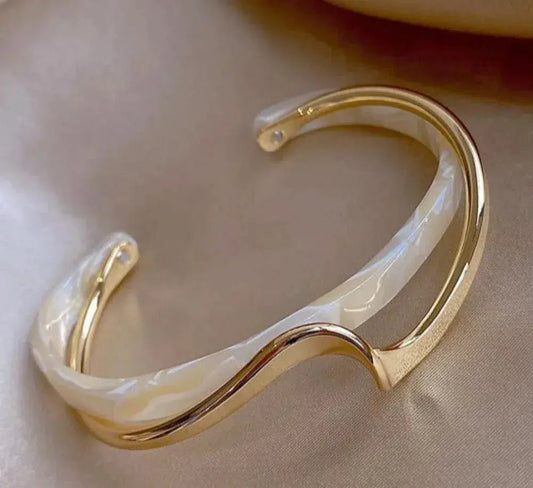 Elegant gold and white resin bracelet on satin background, featuring a modern wave design. Fashion jewelry, stylish accessory, luxury wristwear.
