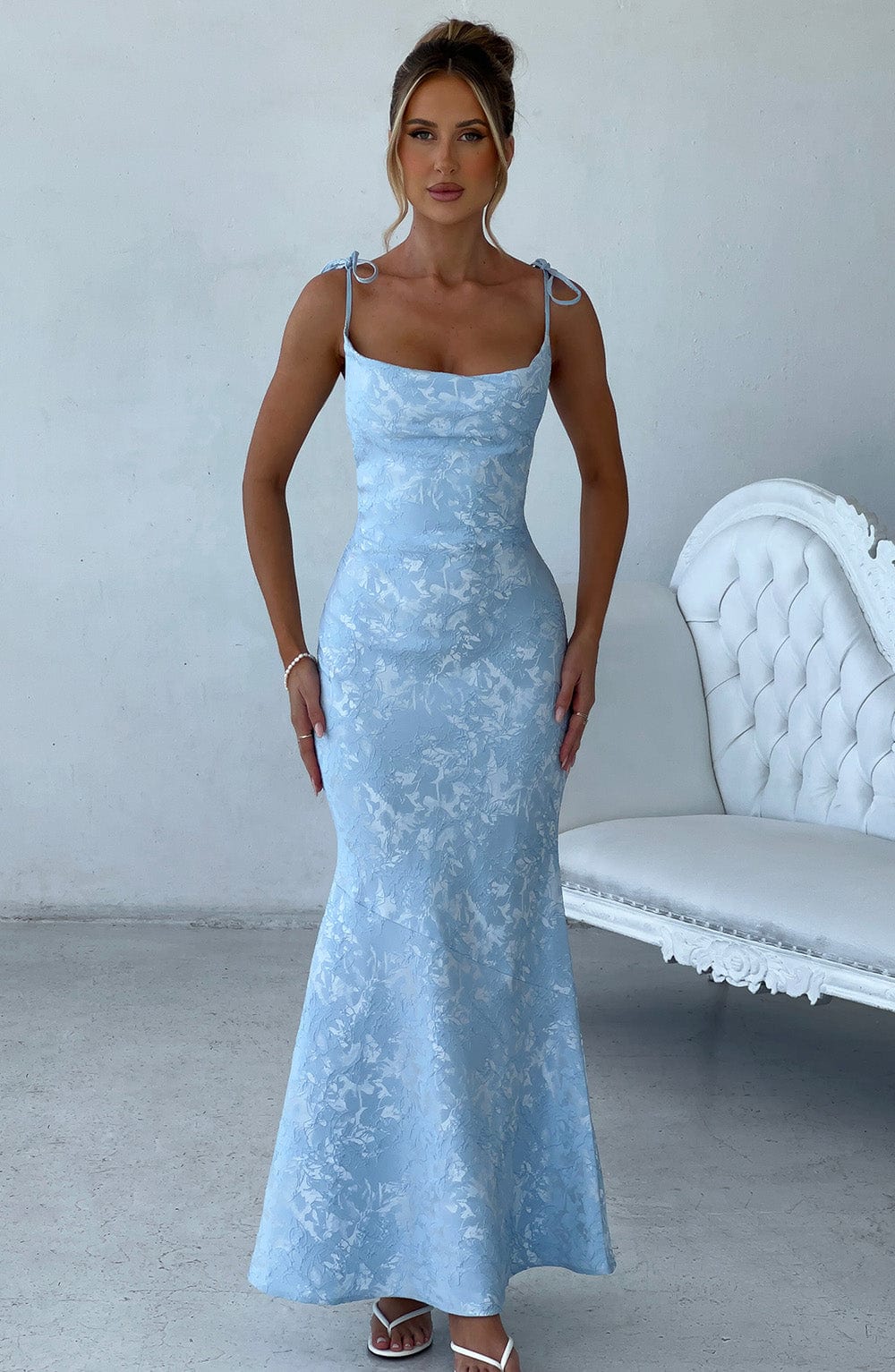 Woman wearing a light blue lace dress in a minimalistic room with a white sofa.